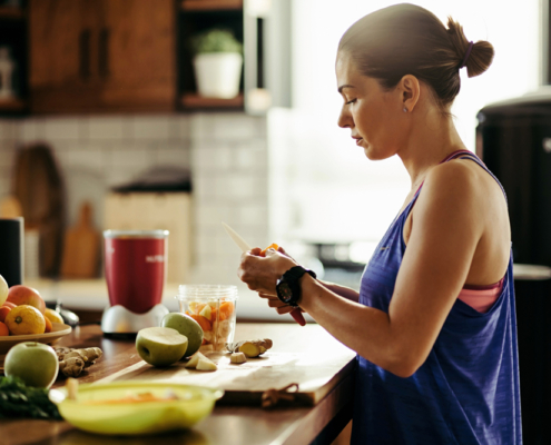 Athletic woman slicing fruit while preparing smoothie in the kitchen.